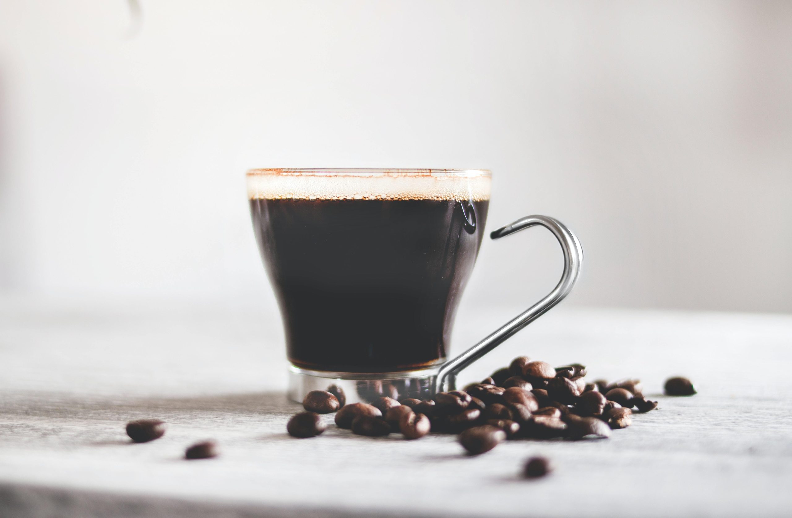 closeup shot of a cup of black coffee on the table with roasted beans under the lights